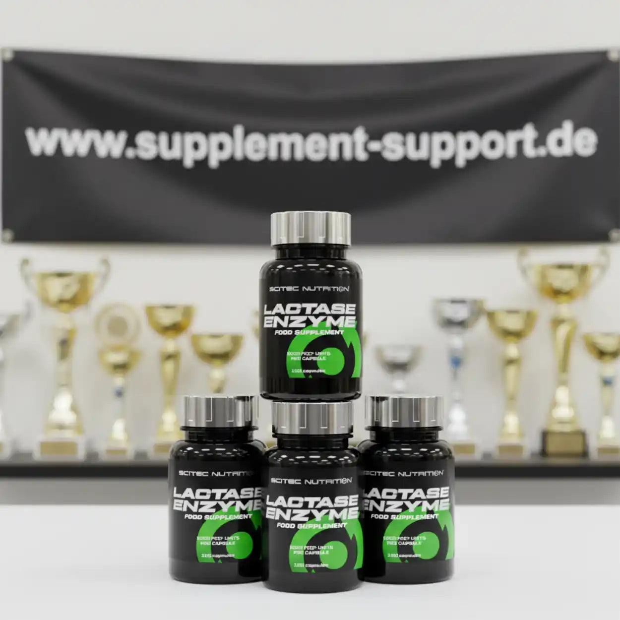 Drei Scitec Nutrition Lactase Enzyme Nahrungsergänzungsmittel-Dosen vor Pokalen und www.supplement-support.de Banner