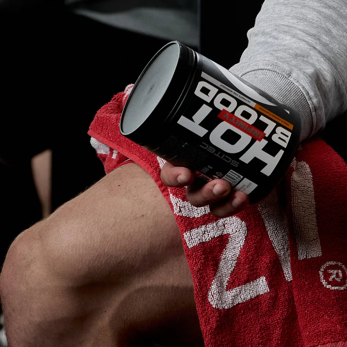 Sportler hält Scitec Nutrition Hot Blood Pre-Workout auf rotem Handtuch im Fitnessstudio