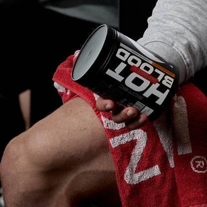 Sportler hält Scitec Nutrition Hot Blood Pre-Workout auf rotem Handtuch im Fitnessstudio