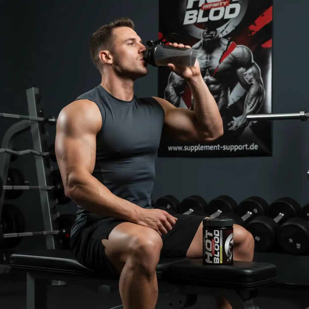 Muskelbepackter Mann trinkt Proteinshake im Fitnessstudio mit Hot Blood Supplement, Hanteln im Hintergrund.