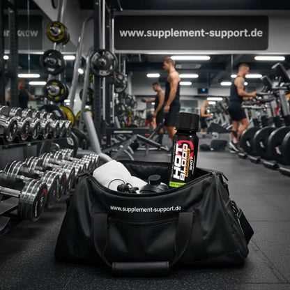 Sporttasche mit Hot Blood Shot und Shaker im Fitnessstudio, Hanteln und Supplement Support Banner im Hintergrund