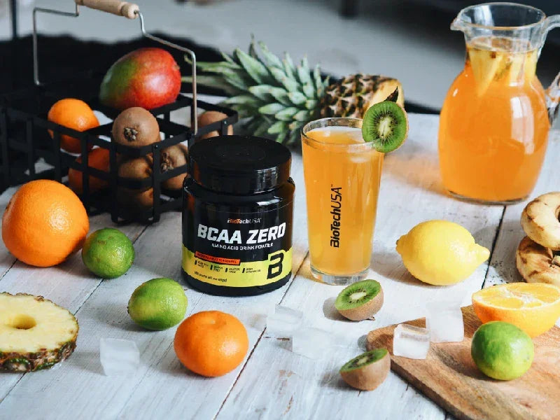 BioTechUSA BCAA Zero Pulver mit Fruchtsaft, Obstsorten und Eiswürfeln auf Holztisch