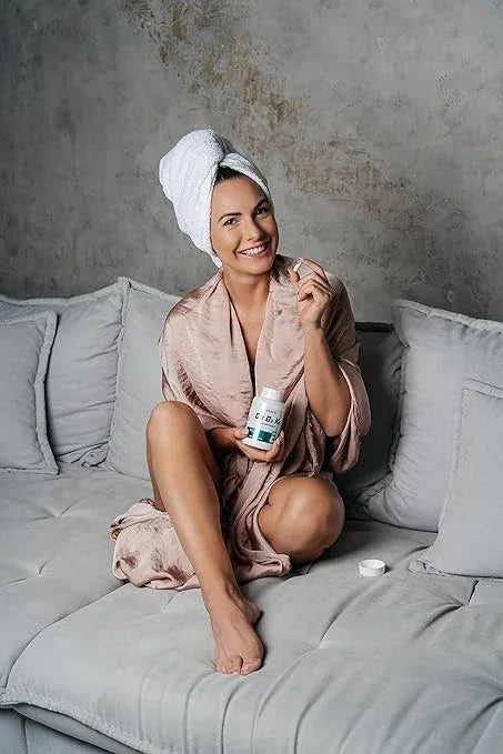 Frau im Bademantel auf Sofa hält Biotech USA CA-D3 K2 Kapseln, Gesundheitsprodukt