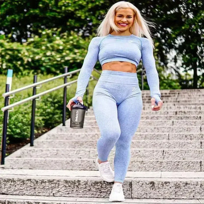 Sportliche Frau in blauer Fitnesskleidung mit Shaker auf Steintreppe im Freien