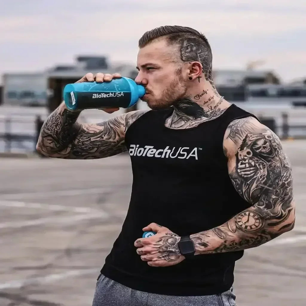 Muskulöser Mann mit Tattoos, BioTechUSA Tanktop und Shaker, Outdoor-Workout-Szene
