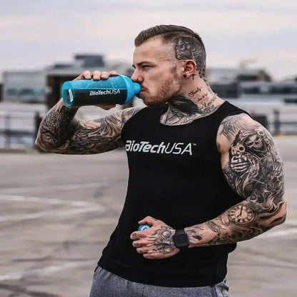 Muskulöser Mann mit Tattoos, BioTechUSA Tanktop und Shaker, Outdoor-Workout-Szene