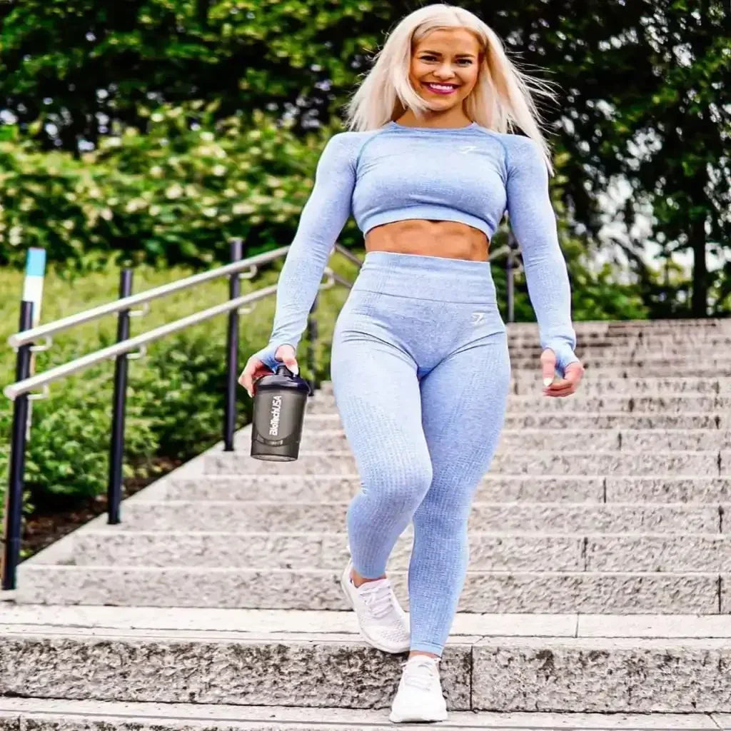 Sportlich gekleidete Frau in blauer Leggings läuft draußen die Treppe hinunter mit Fitness-Shaker