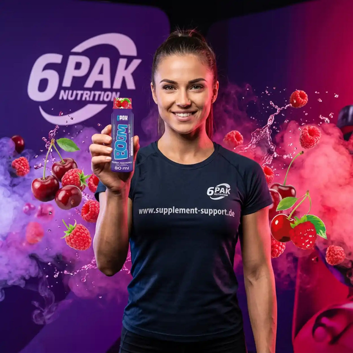 Frau hält TREC NUTRITION BOOM Pre Workout Shot vor violettem Hintergrund mit Kirschen und Beeren.
