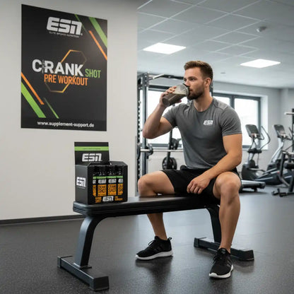 Mann trinkt ESN Crank Shot Pre Workout im Fitnessstudio, neben ihm Packung mit Booster-Shots