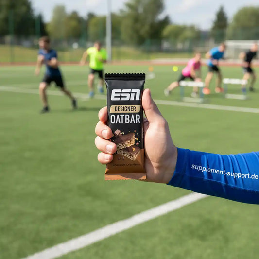Designer Oatbar Riegel Schoko-Geschmack, gehalten vor Sportlern auf Fußballfeld