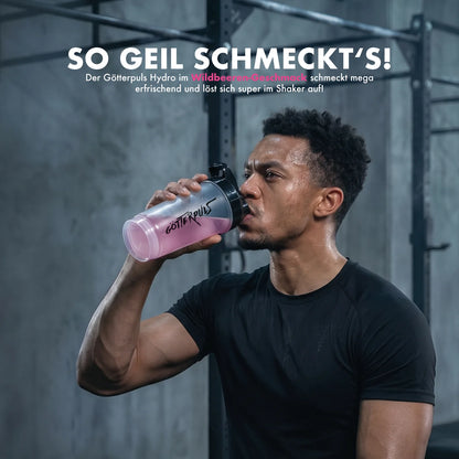 Athlet trinkt pinken Göttpuls Hydro Wildbeeren-Shake aus Shaker im Fitnessstudio