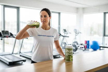 Frau trinkt grünen Protein-Shake im Fitnessstudio, neben Protein Iced Matcha Latte Dose