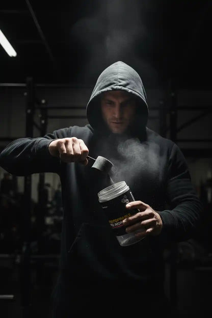 Mann im Hoodie mischt Proteinpulver in Gym – Sportnahrung & Booster für Training